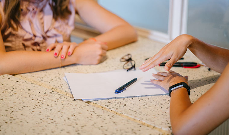 Women sitting across desk discussing work.